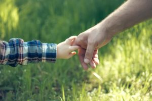 male hand of father lead his child son in summer green grass nature outdoor, trust family concept